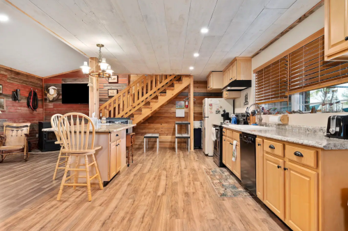 Cozy kitchen and living area with wooden floors, a staircase, and modern appliances in a rustic setting.